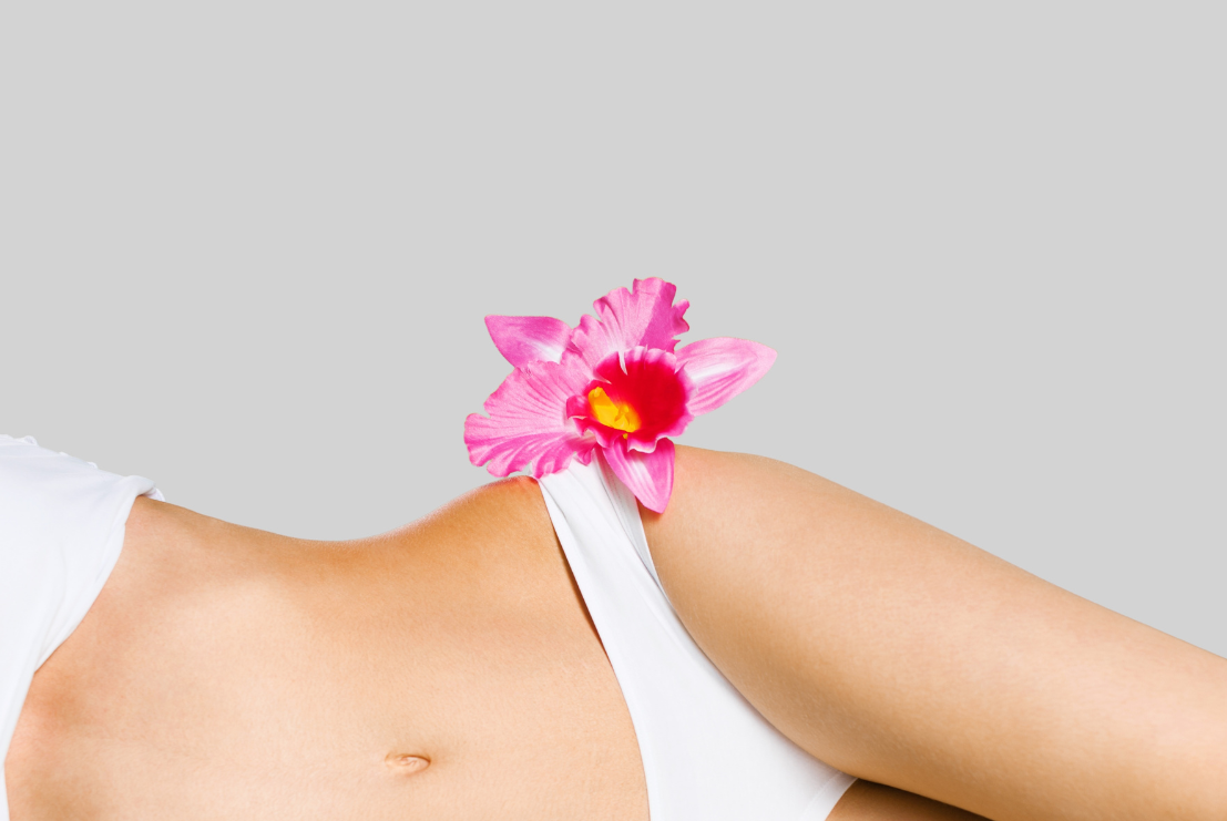 Sievietes ķermeņa vidusdaļa - vēders, gurni un uz gurna ir novietots rozā zieds simbolizējot intīmās mikrofloras līdzsvaru